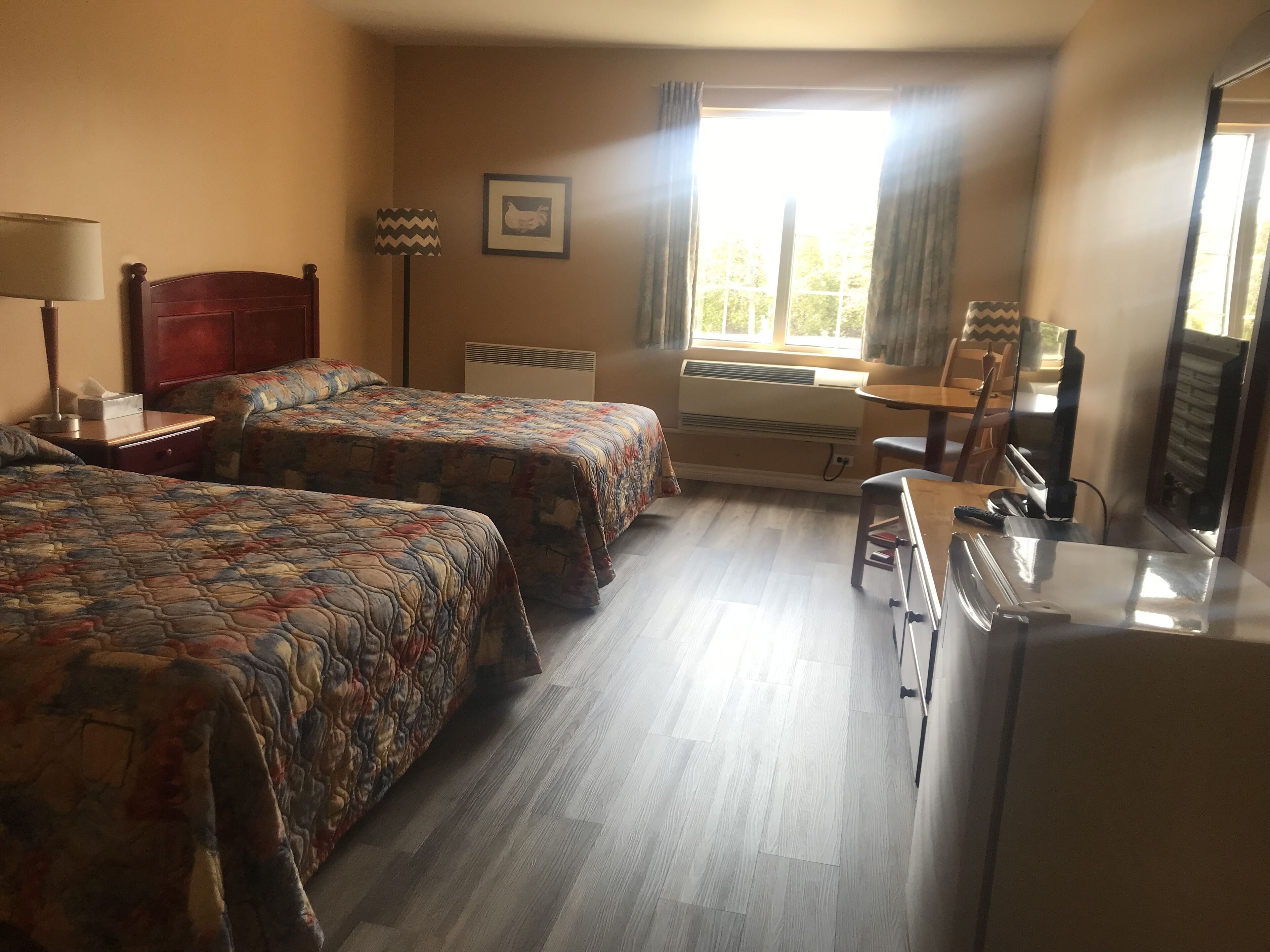 A hotel room with two beds, a desk, a chair, a lamp, an air conditioner, and a window with curtains.