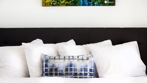 Una cama con ropa blanca y un único cojín decorativo de diseño azul y blanco.
