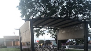 Un patio exterior con pérgola, asientos y un hogar para la chimenea.