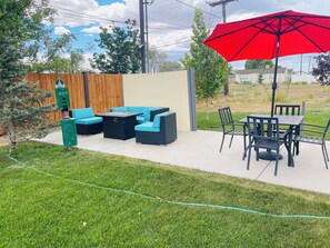 An outdoor patio with a table and chairs, a red umbrella, and a small garden area.