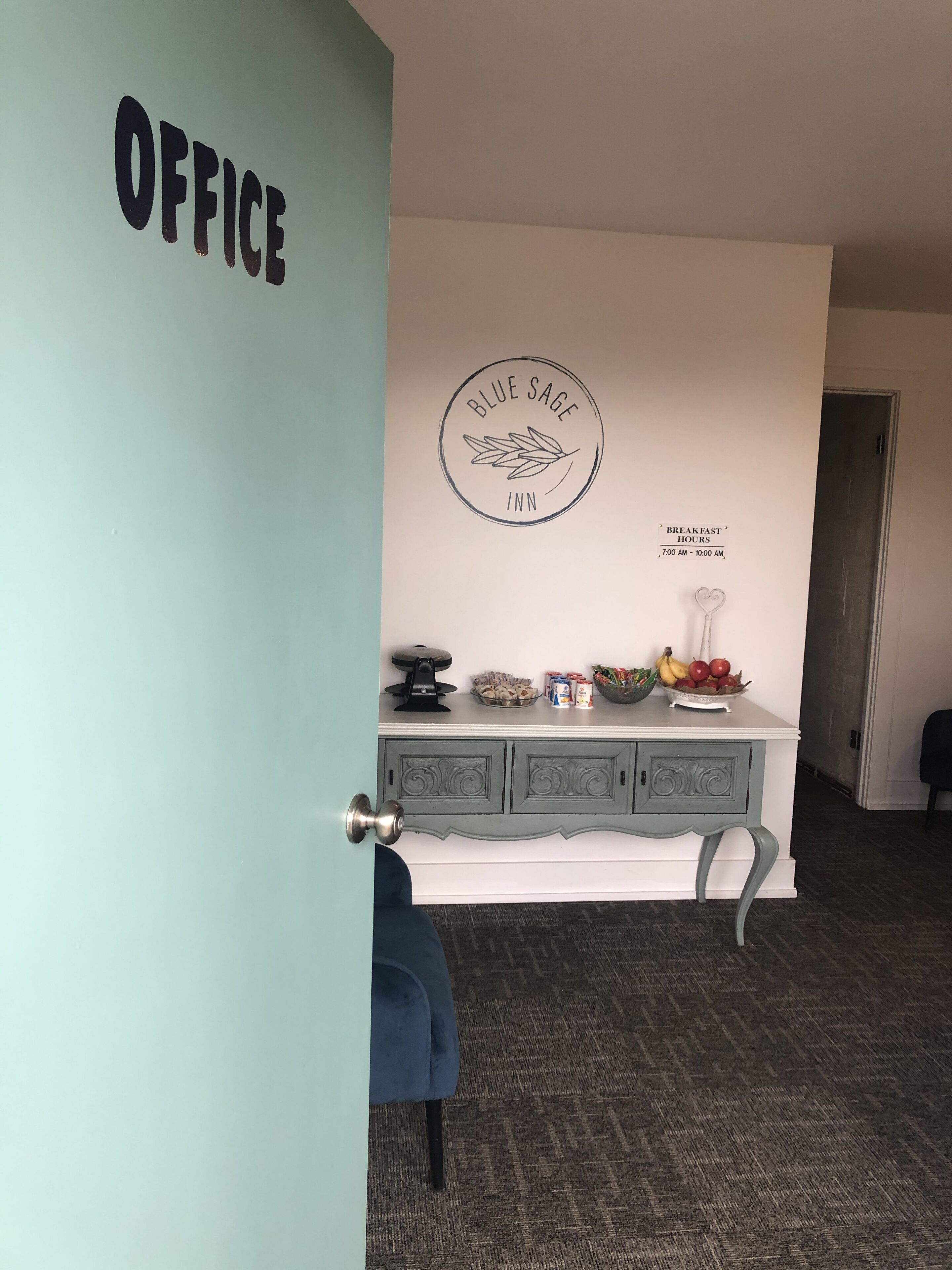 Et værelse med et skrivebord, et skilt på væggen med teksten "OFFICE" og et skilt, der angiver "Morgenmadsåbningstider 7:00 - 10:00".