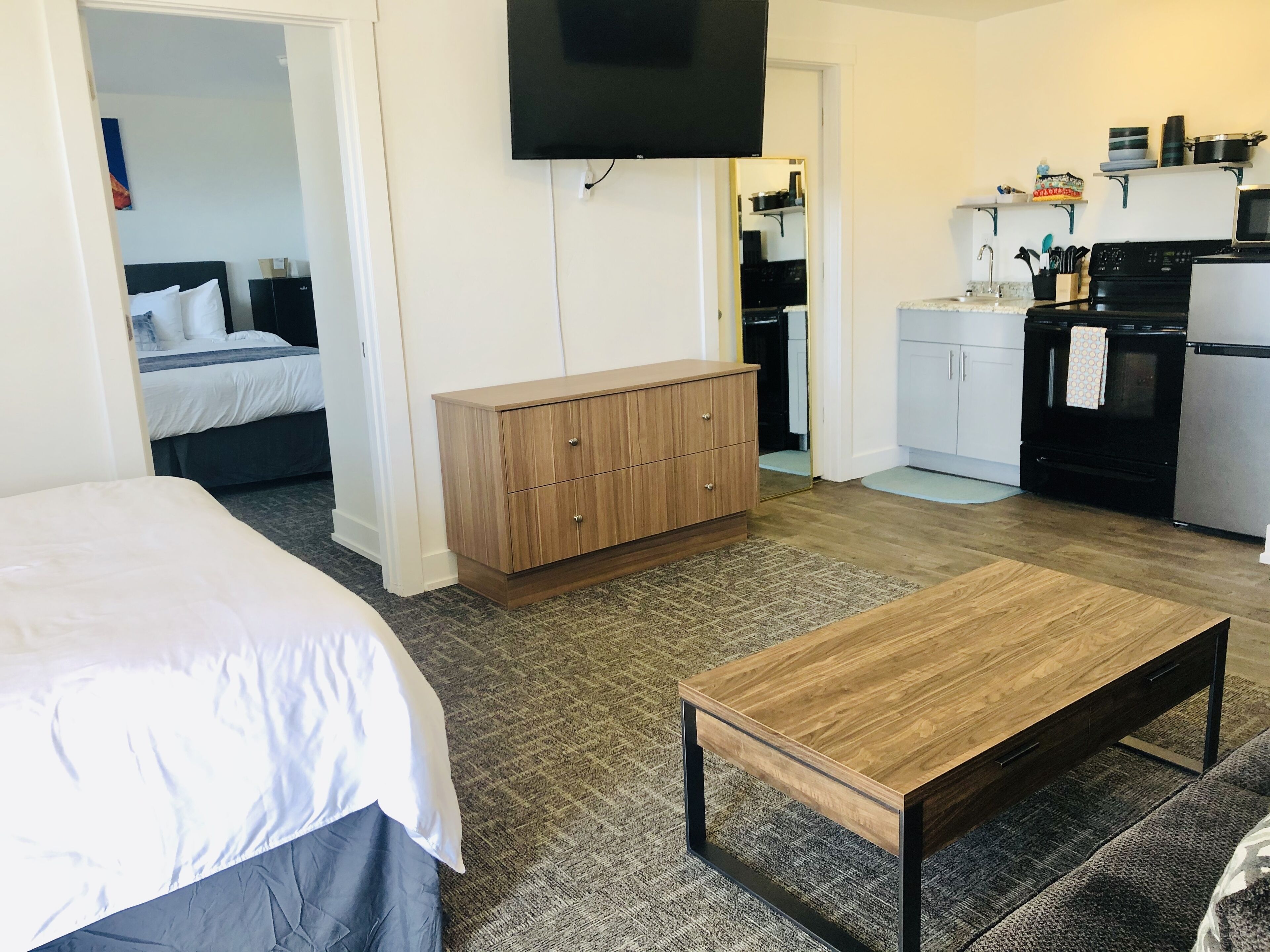 Quarto de hotel com uma cama, um armário de madeira, uma televisão, uma cozinha compacta com fogão e frigorífico, e piso coberto de carpete.