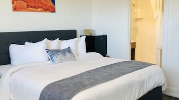 A neatly made bed with white and gray bedding, a dark headboard, and a painting of a red rock formation on the wall.