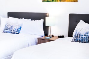 A hotel room with two beds, white bedding, and a nightstand with a lamp and a clock.