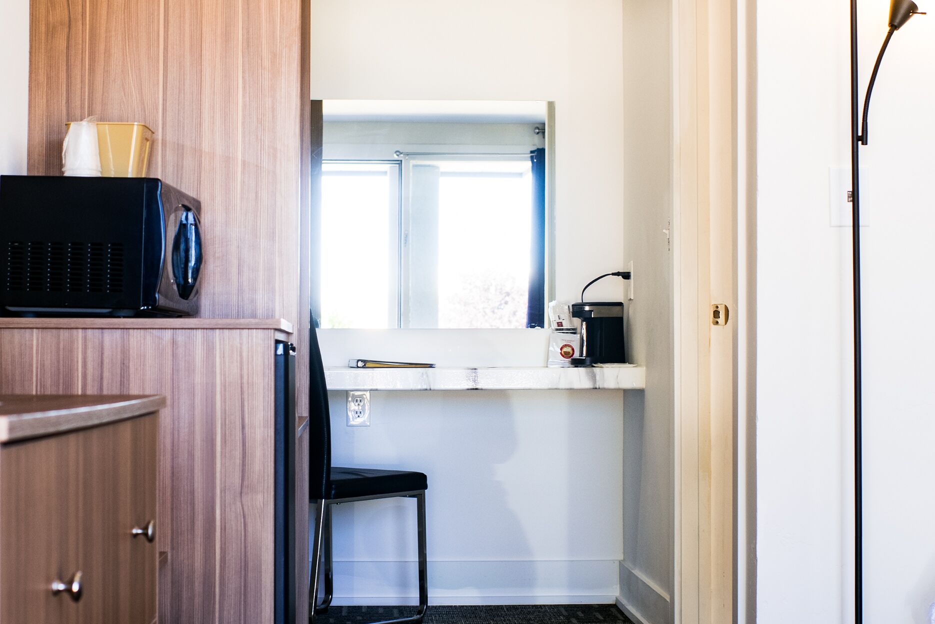 A compact kitchenette with a microwave, a coffee maker, and a small window.