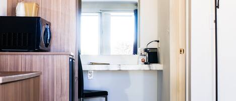 A compact kitchenette with a microwave, a coffee maker, and a small window.