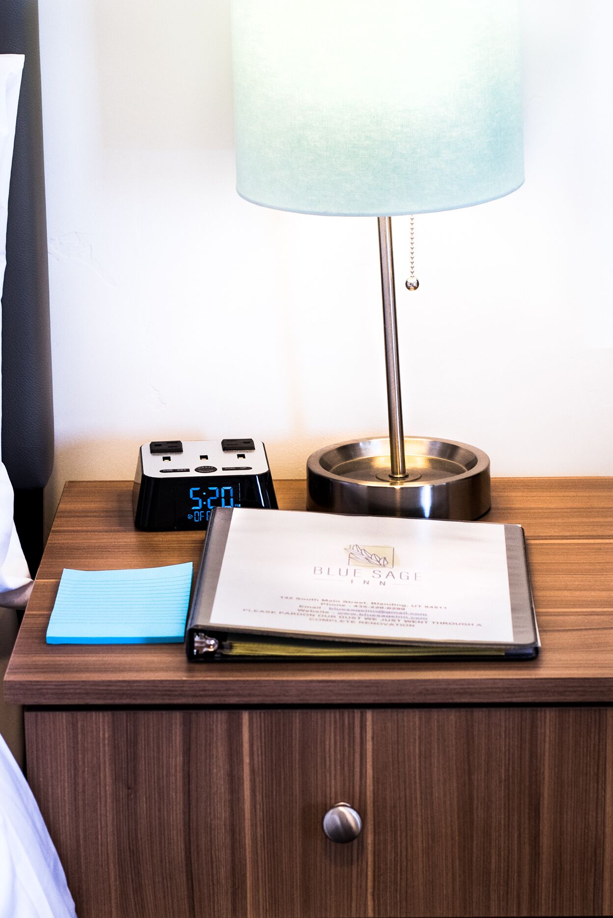 Un comodino in legno con una sveglia digitale, una lampada e una tessera chiave per la camera d'albergo.