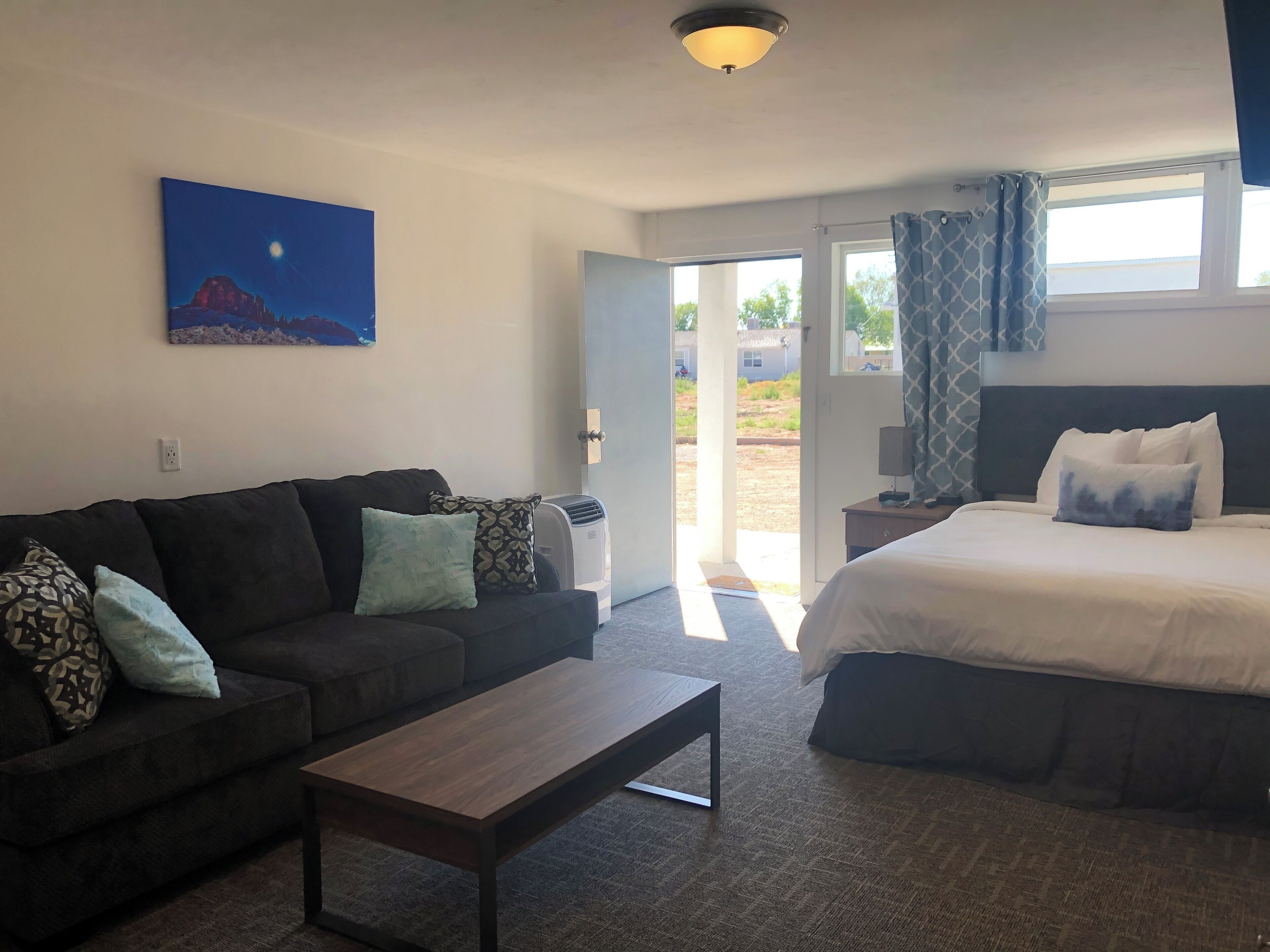 Una habitación de hotel con cama, sofá, una mesita de centro y un cuadro en la pared.