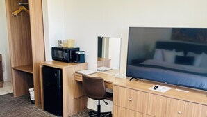 Habitación de hotel con escritorio de madera, silla de oficina negra, televisor, microondas y un refrigerador pequeño.