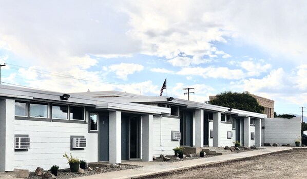 A row of single-story buildings with a flat roof, each featuring a small porch and a flagpole with an American flag.