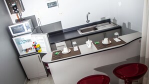 A compact kitchen with a microwave, sink, and two red bar stools. - Apart Hotel El Peregrino (Abancay)