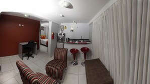A compact living space with a kitchenette, a dining area with red bar stools, and a striped sofa set. - Apart Hotel El Peregrino (Abancay)