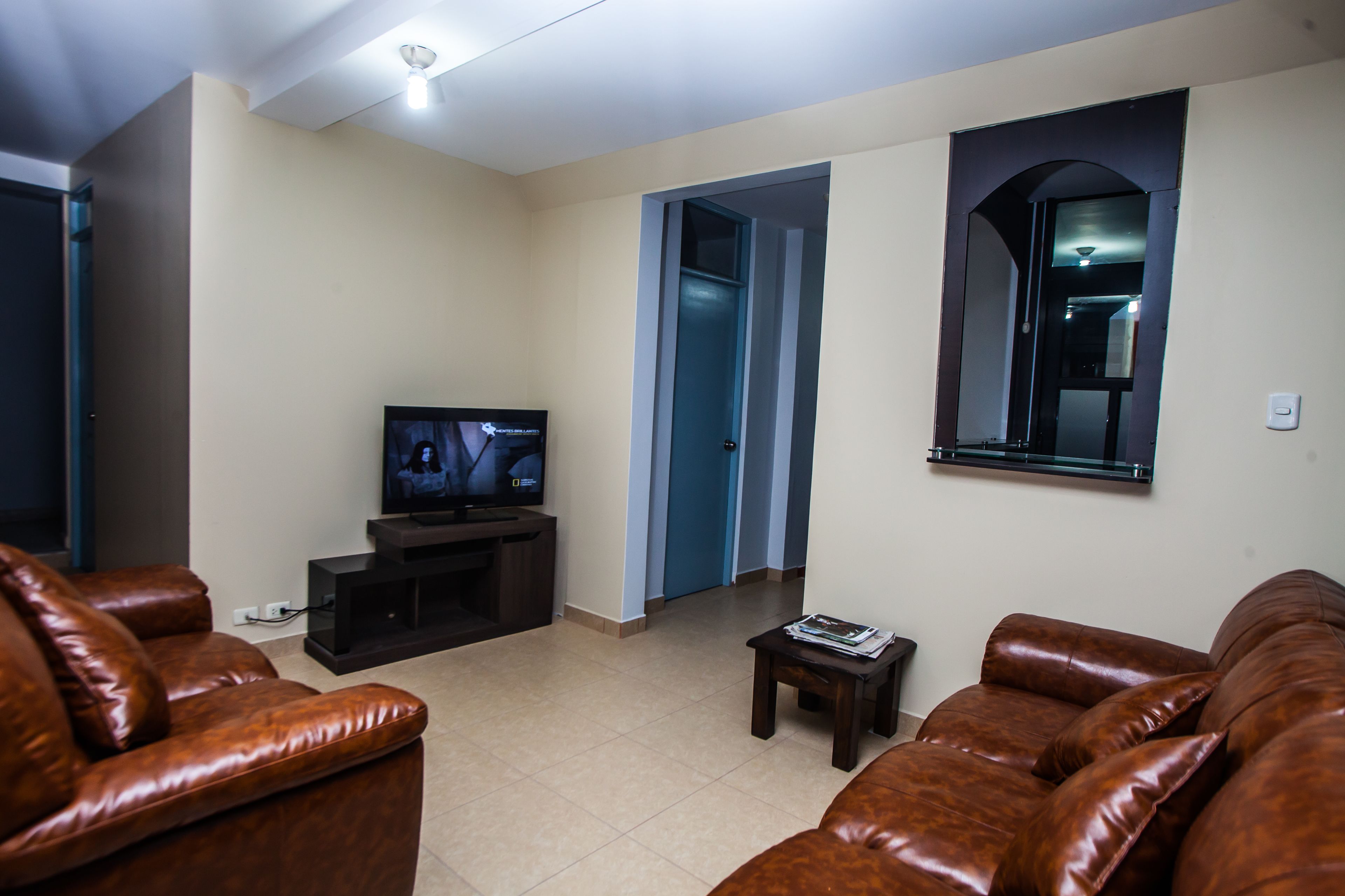 A living room with a television, leather sofas, a small table, and a doorway leading to another room.
