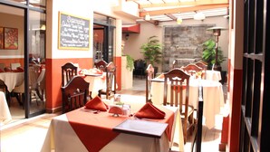 A restaurant with tables set for dining, a menu board, and a stone wall in the background. - Apart Hotel El Peregrino (Abancay)