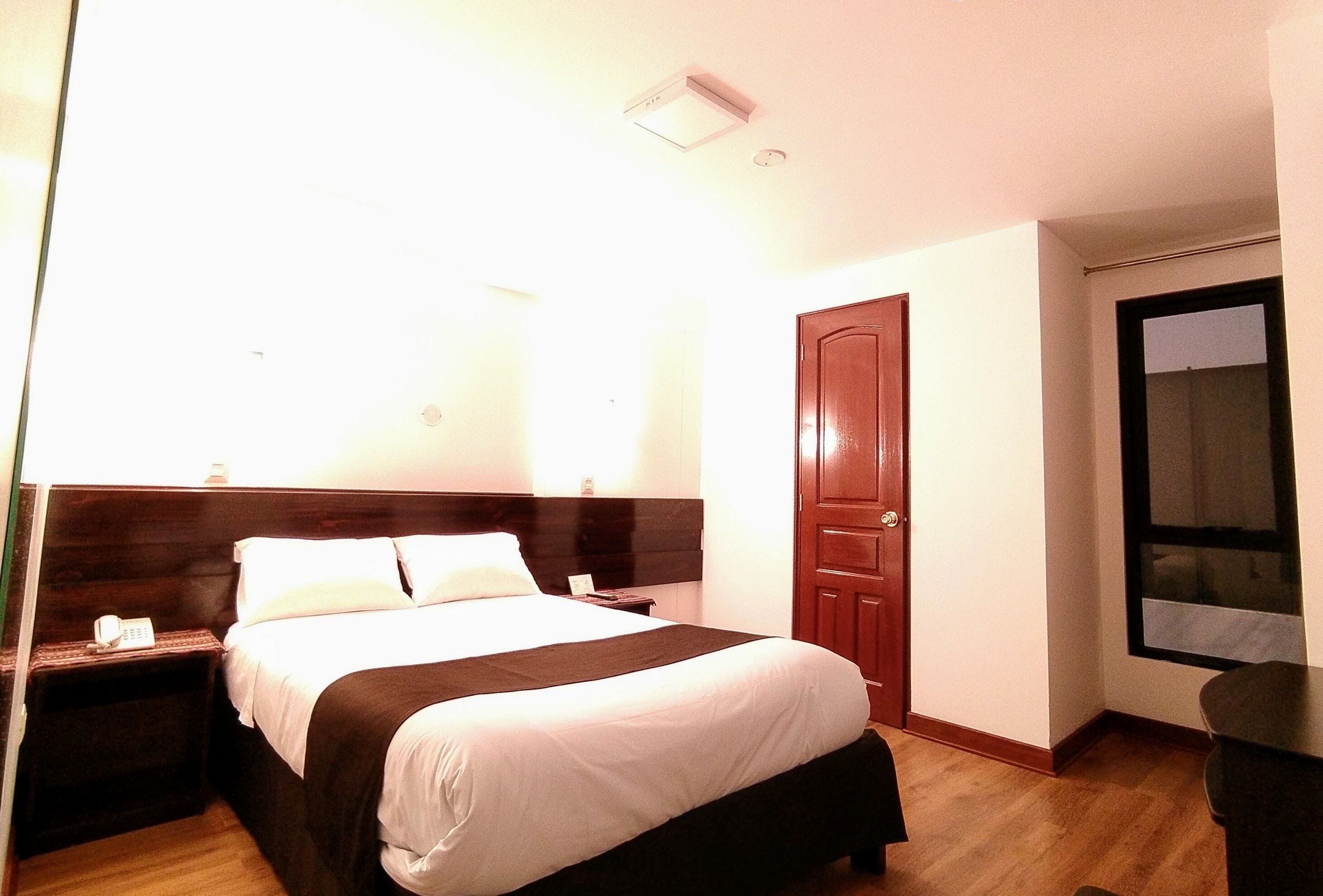 A hotel room with a bed, bedside table, and a door.