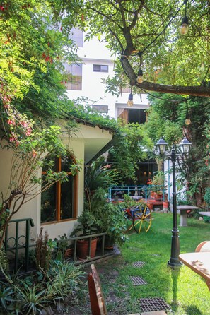 A garden with a house, potted plants, a bicycle, and a lamp post. - Illas Inn (Cusco)