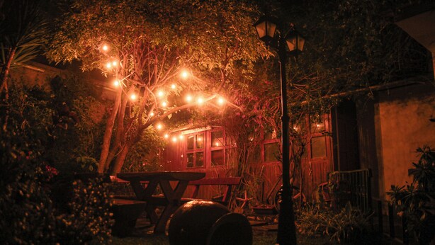 A rustic outdoor setting with a wooden picnic table, barrels, and string lights. - Illas Inn (Cusco)