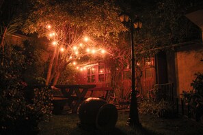 A rustic outdoor setting with a wooden picnic table, barrels, and string lights. - Illas Inn (Cusco)