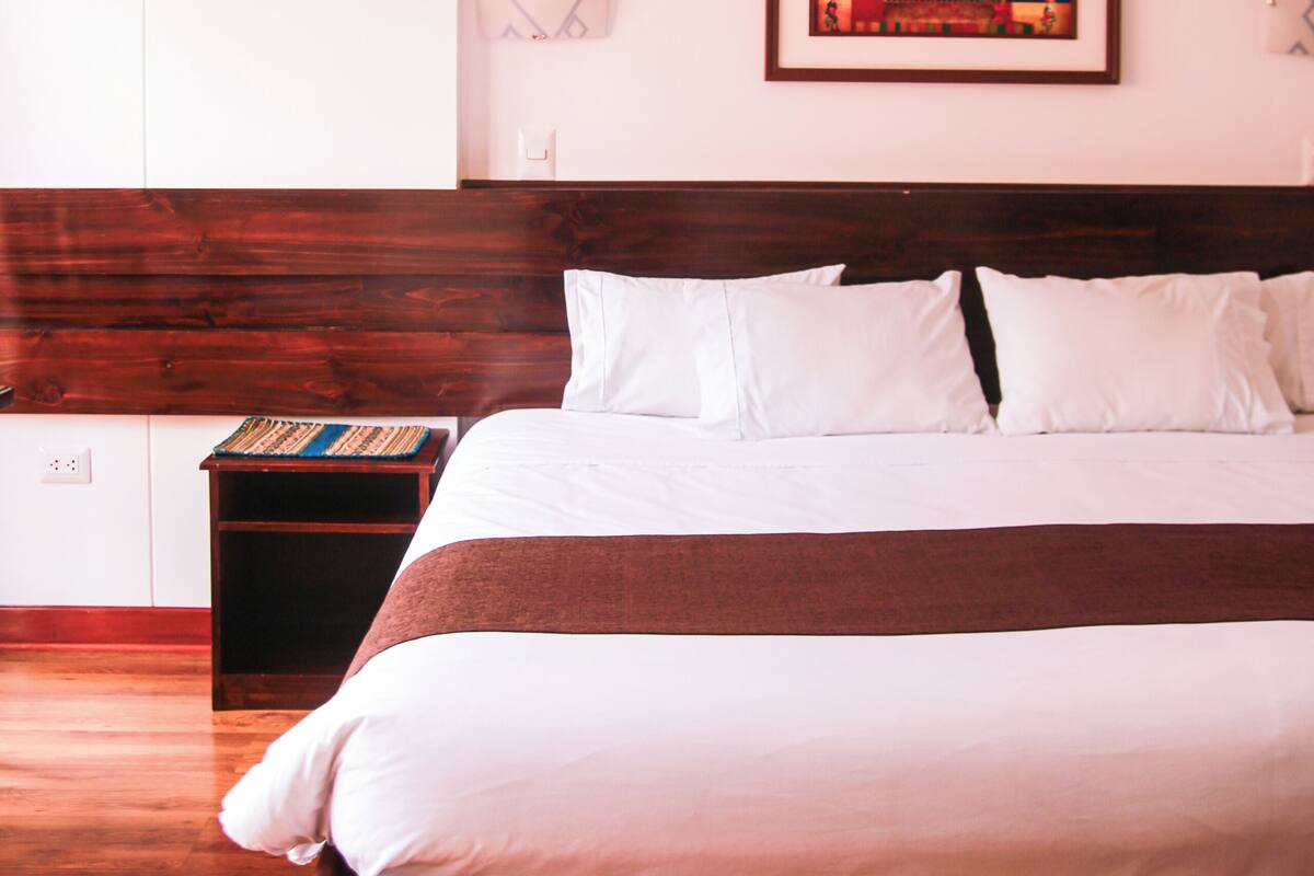 A neatly made bed with white and brown bedding, a wooden headboard, and a small bedside table with a book.