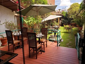An outdoor patio with wooden tables and chairs, umbrellas, and potted plants. - Illas Inn (Cusco)
