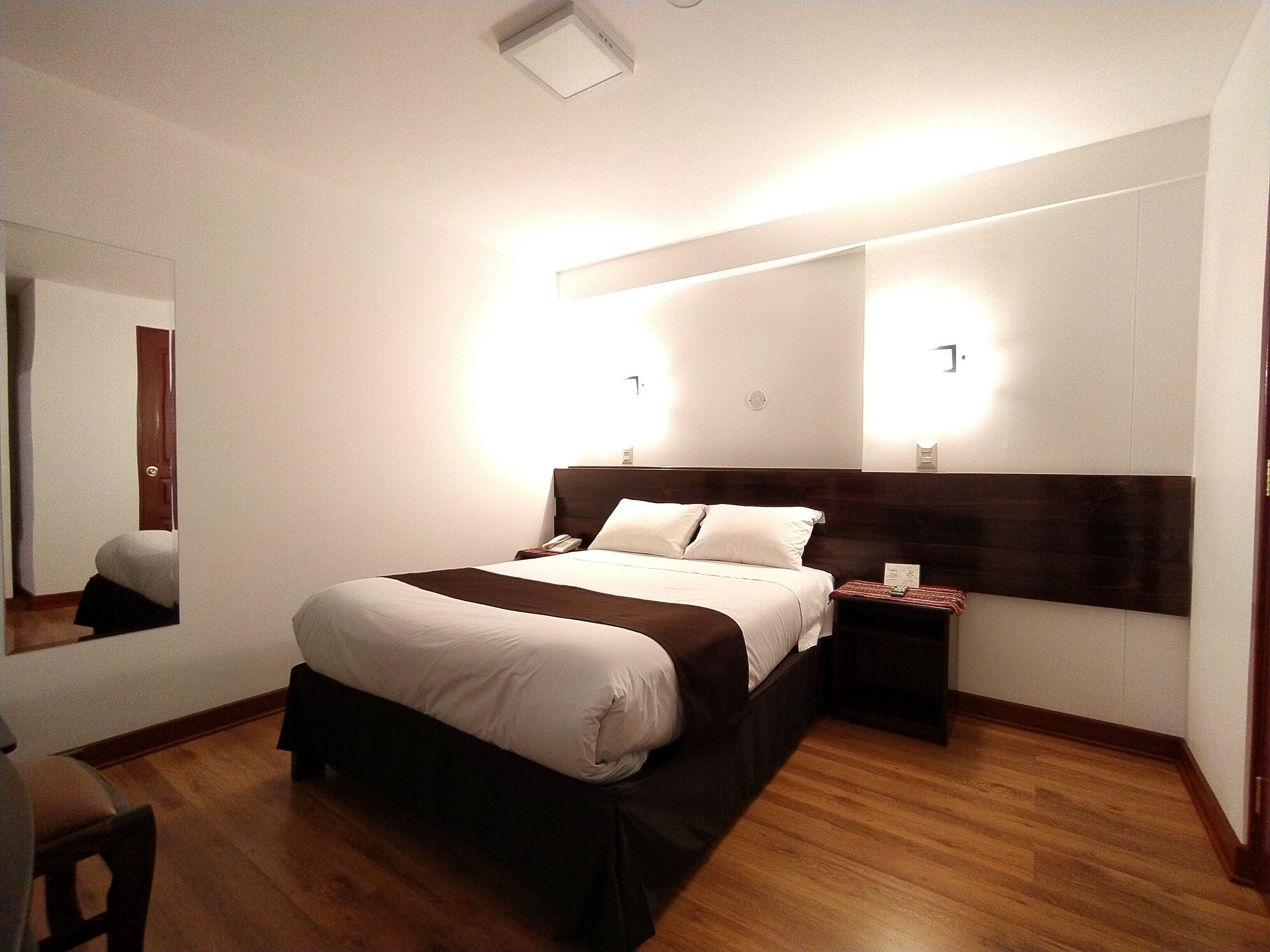 Habitación de hotel con una cama grande, mesitas de noche, un espejo y suelo de madera.