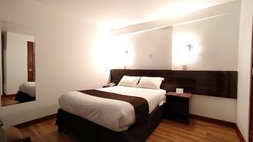 Habitación de hotel con una cama grande, mesitas de noche, un espejo y suelo de madera.