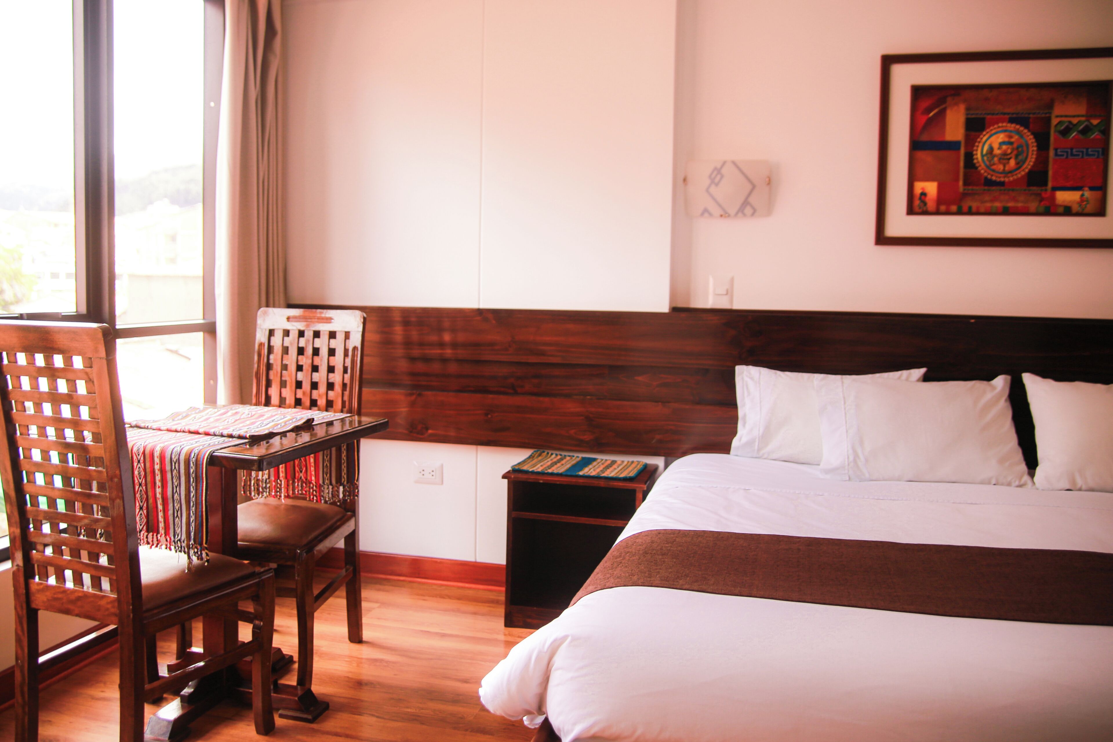 Habitación de hotel con cama y silla de madera, una mesita y una ventana con cortinas.