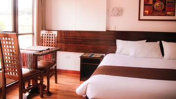 Habitación de hotel con cama y silla de madera, una mesita y una ventana con cortinas.