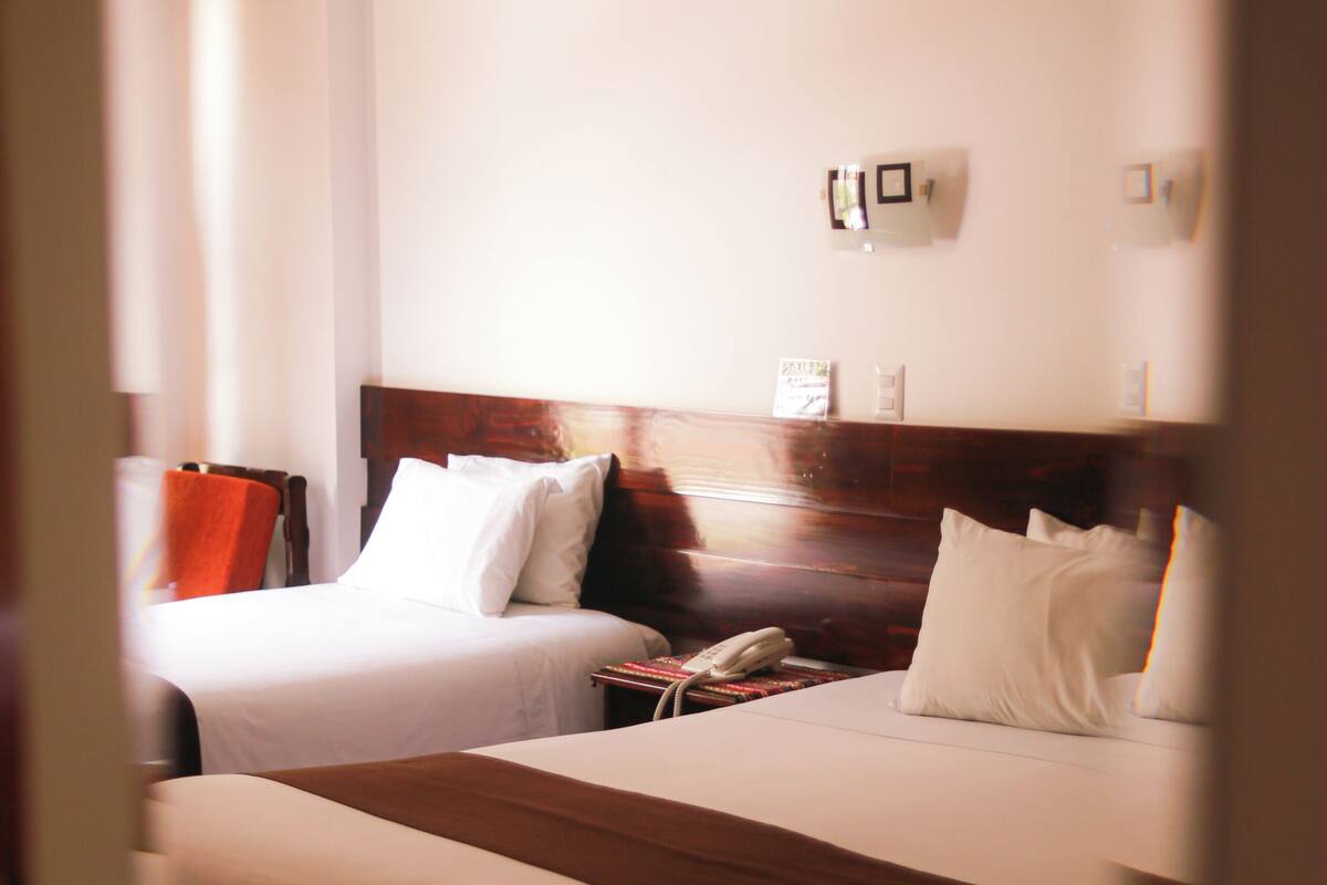 A hotel room with two beds, a wooden headboard, a bedside table with a telephone, and a wall-mounted light fixture.