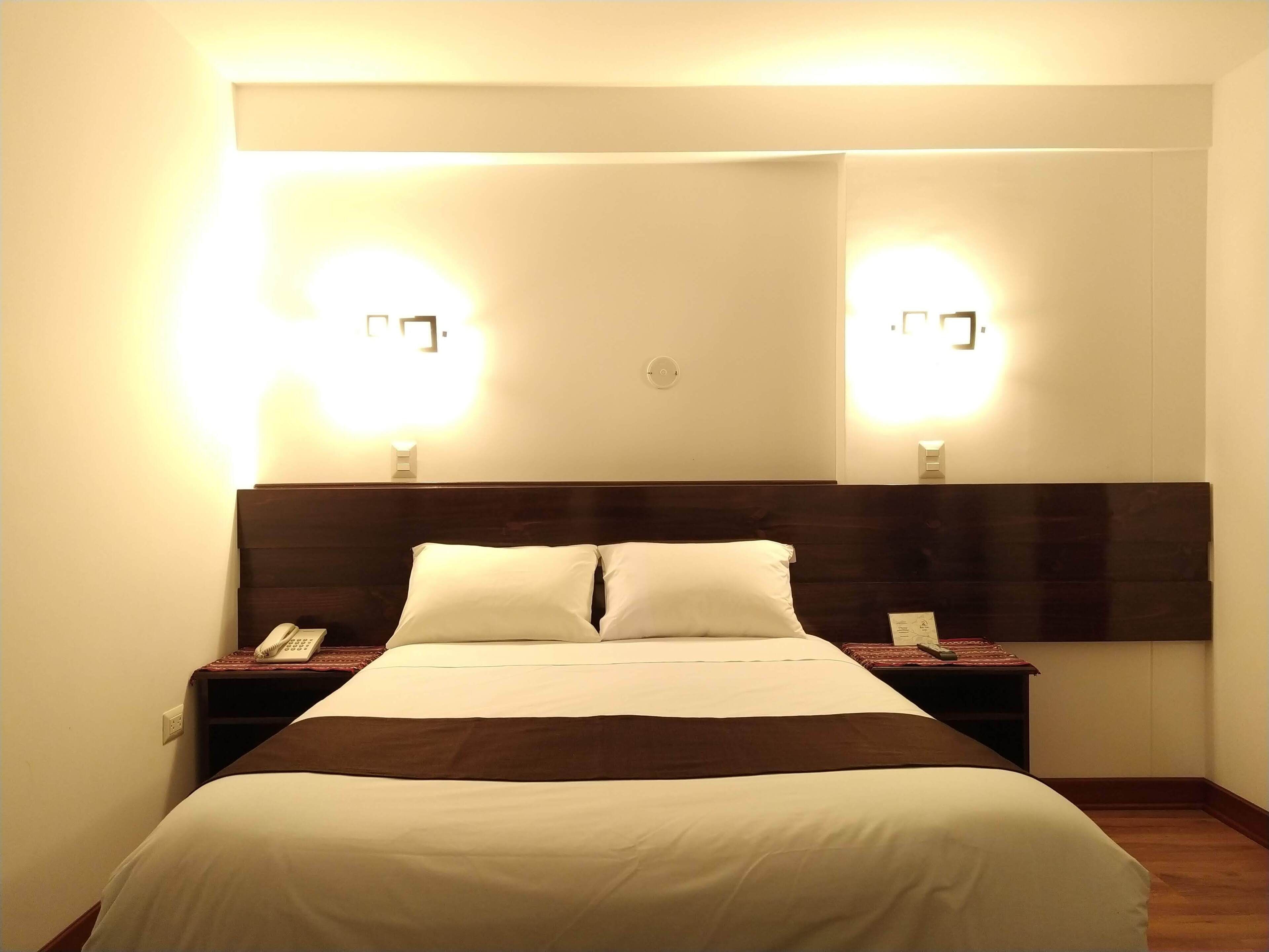 A hotel room with a large bed, two bedside tables, and wall-mounted lights.