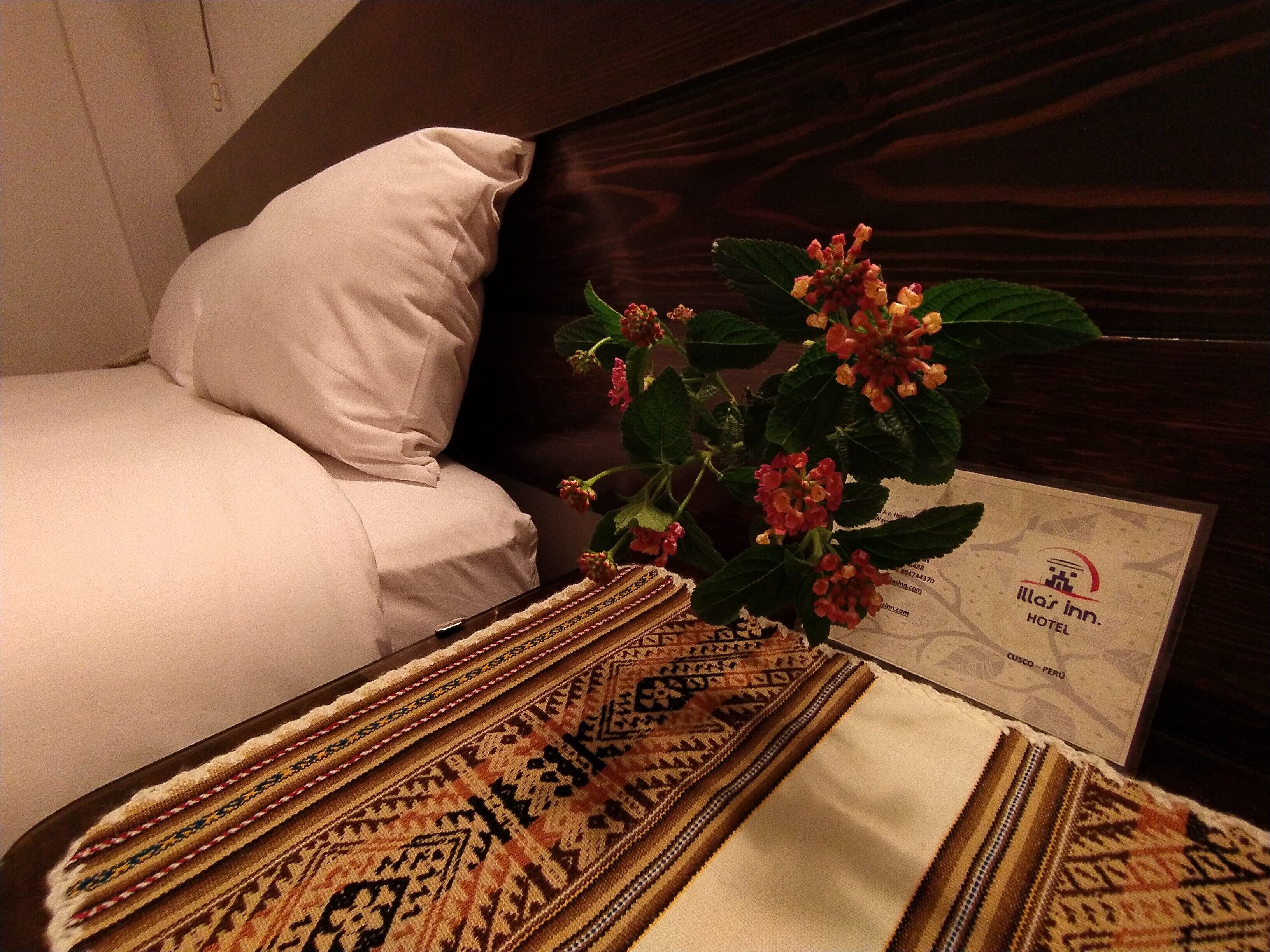 Una habitación de hotel con una cama, un tapete estampado y una planta con flores rojas.