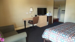 Quarto de hotel com cama, escrivaninha, cadeira, televisão, micro-ondas e luminária.