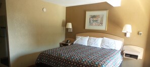 Habitación de hotel con cama, dos lámparas de noche, mesita de noche, teléfono y un cuadro en la pared.