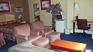 Quarto de hotel com uma cama, dois sofás, uma mesinha, uma escrivaninha com cadeira, televisão e um vaso de planta.