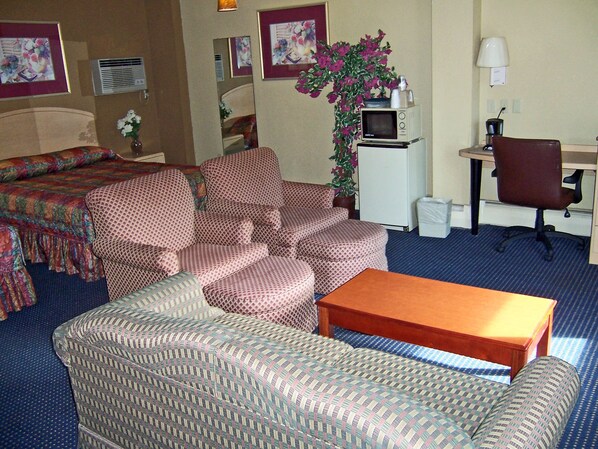 Habitación de hotel con cama, dos sofás, una mesita, escritorio con silla, televisor y planta en maceta.