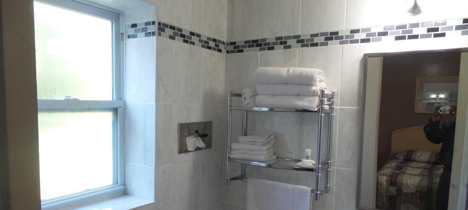Un baño con cabina de ducha de vidrio, un perchero con toallas dobladas y una ventana que proporciona luz natural.