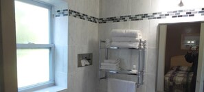 Un baño con cabina de ducha de vidrio, un perchero con toallas dobladas y una ventana que proporciona luz natural.