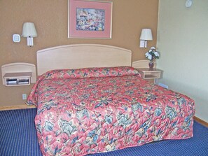 A hotel room with a floral bedspread, two bedside tables with lamps, a small shelf, and a framed picture on the wall.