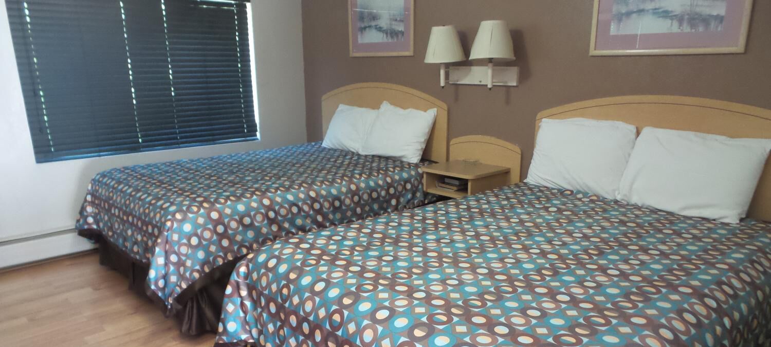 Une chambre d’hôtel avec deux lits, chacun agrémenté de draps à motifs, une table de chevet et des lampes fixées au mur.