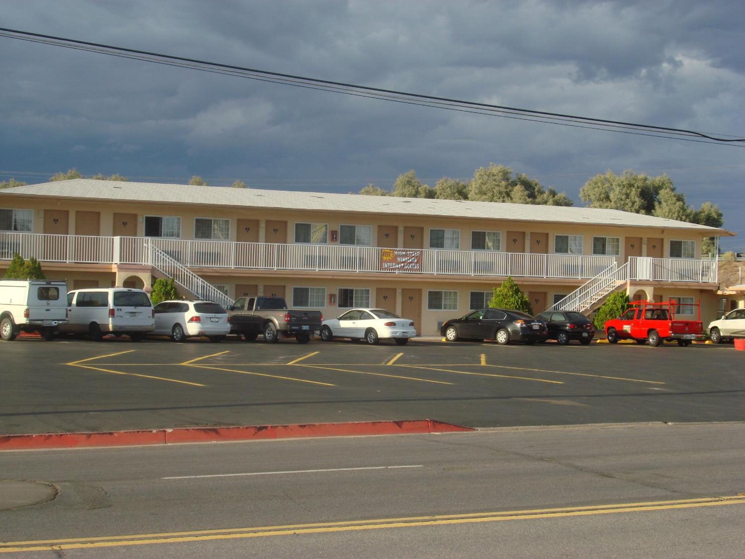 Un motel con struttura su due piani, un parcheggio con diverse auto e un balcone con ringhiera.