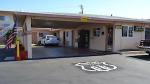 Un motel con un letrero claro que indica la habitación 2104, una bandera estadounidense y un cartel que dice 'Welcome to Route 66' en el estacionamiento.
