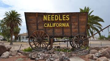 Un carro de madera con la inscripción "NEEDLES CALIFORNIA", rodeado de rocas y palmeras.