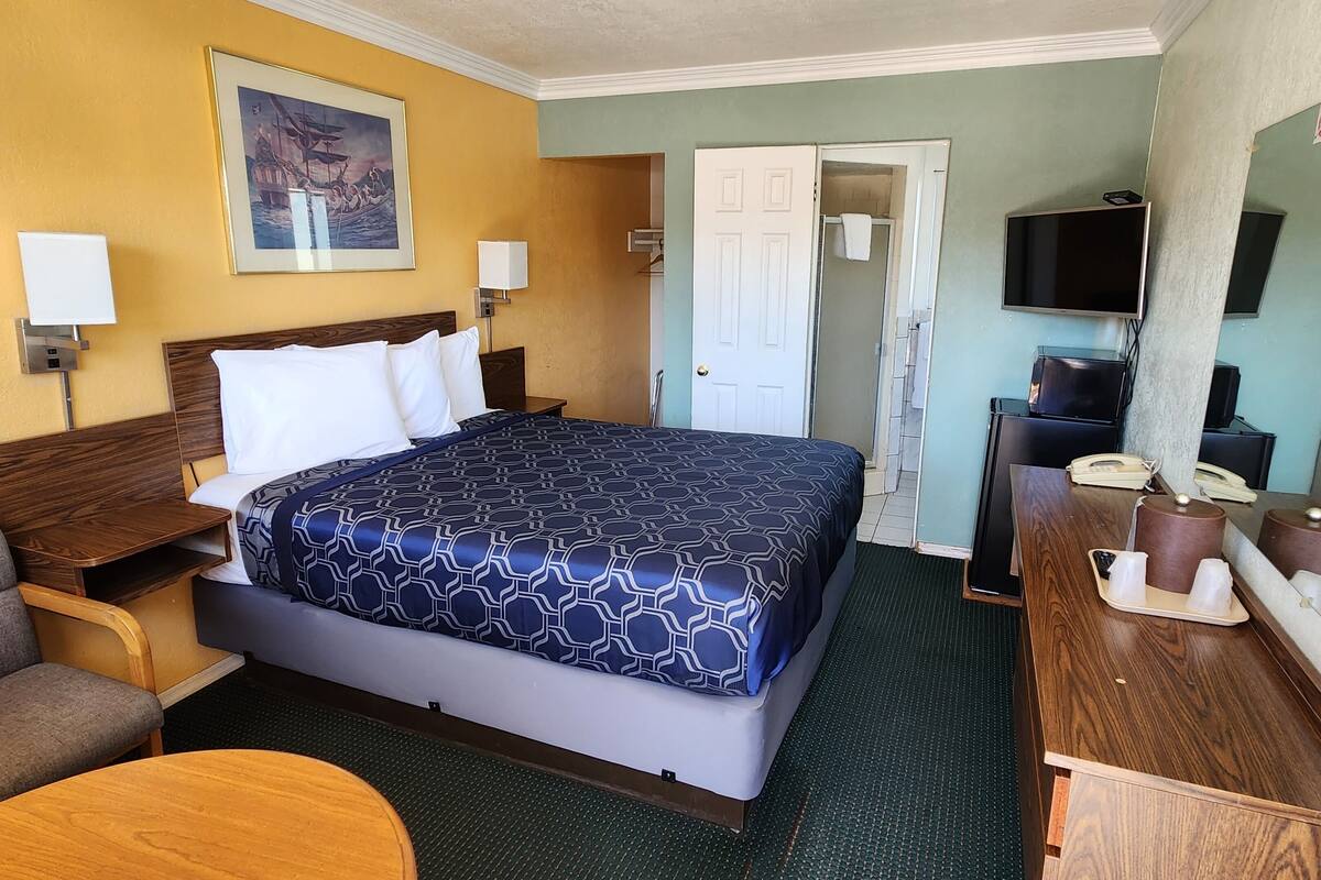 Une chambre d’hôtel avec un grand lit, un bureau avec un ordinateur, une télévision et un tableau au mur.