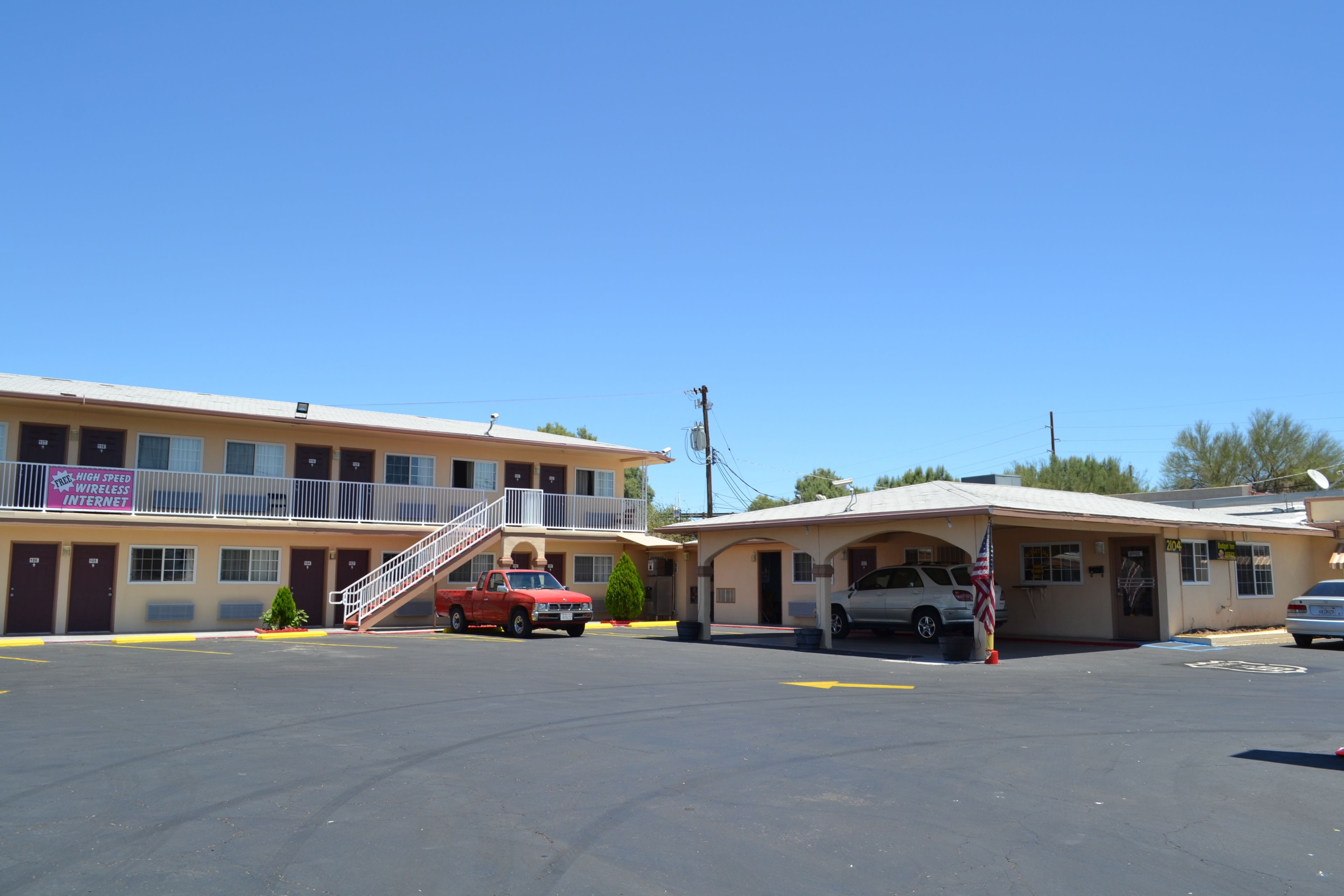 Un motel con un edificio de dos pisos, una zona de estacionamiento techada y una camioneta roja estacionada al frente.