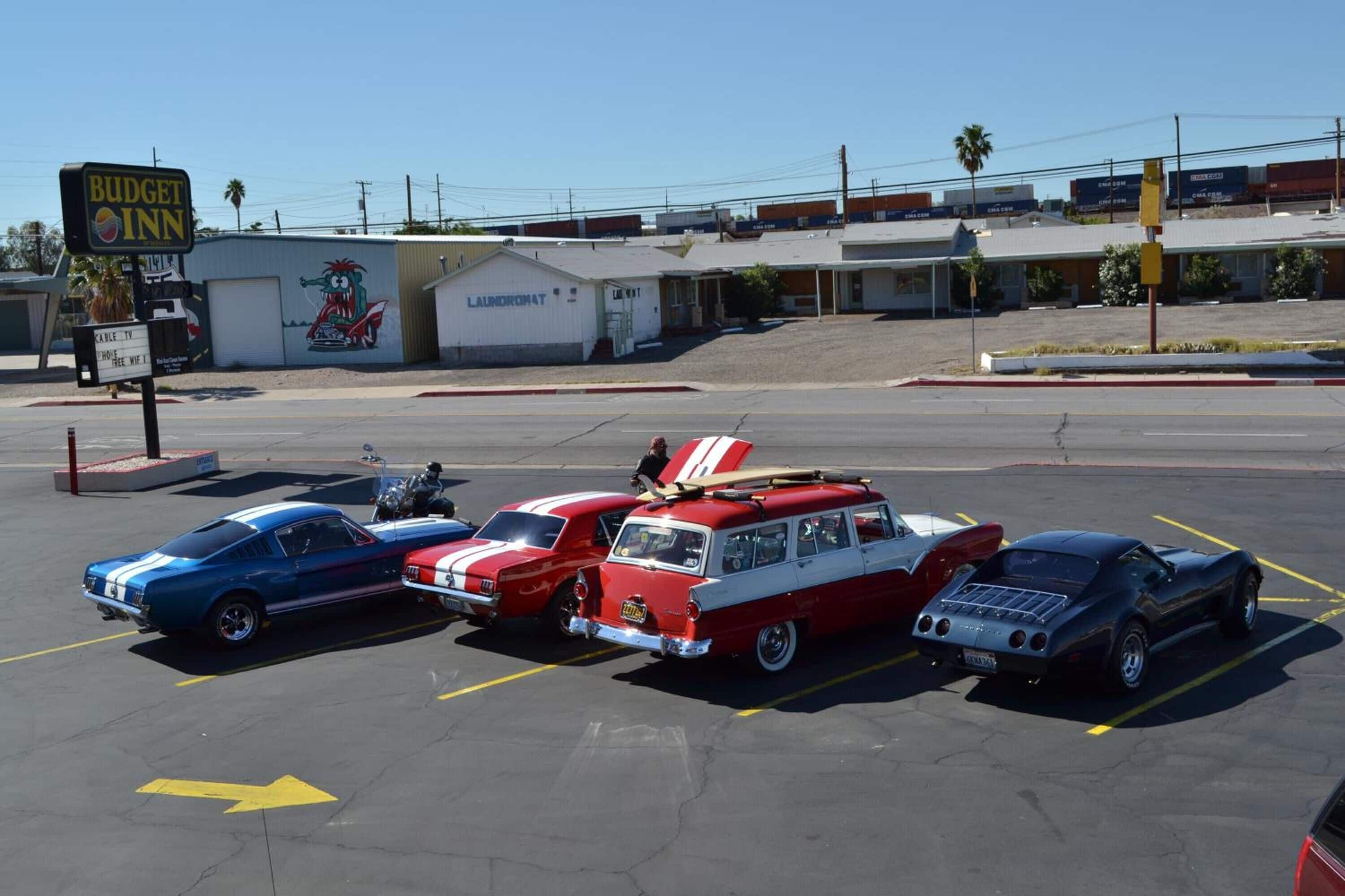 A parking lot with vintage cars, a laundromat, and a Budget Inn sign.