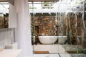 Un baño moderno con pared de piedra, una bañera independiente y cabina de ducha de vidrio.