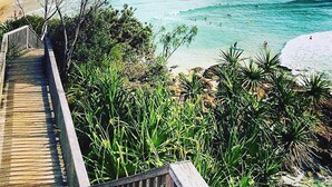 Una pasarela de madera que conduce a una playa con aguas turquesas cristalinas y una orilla arenosa.