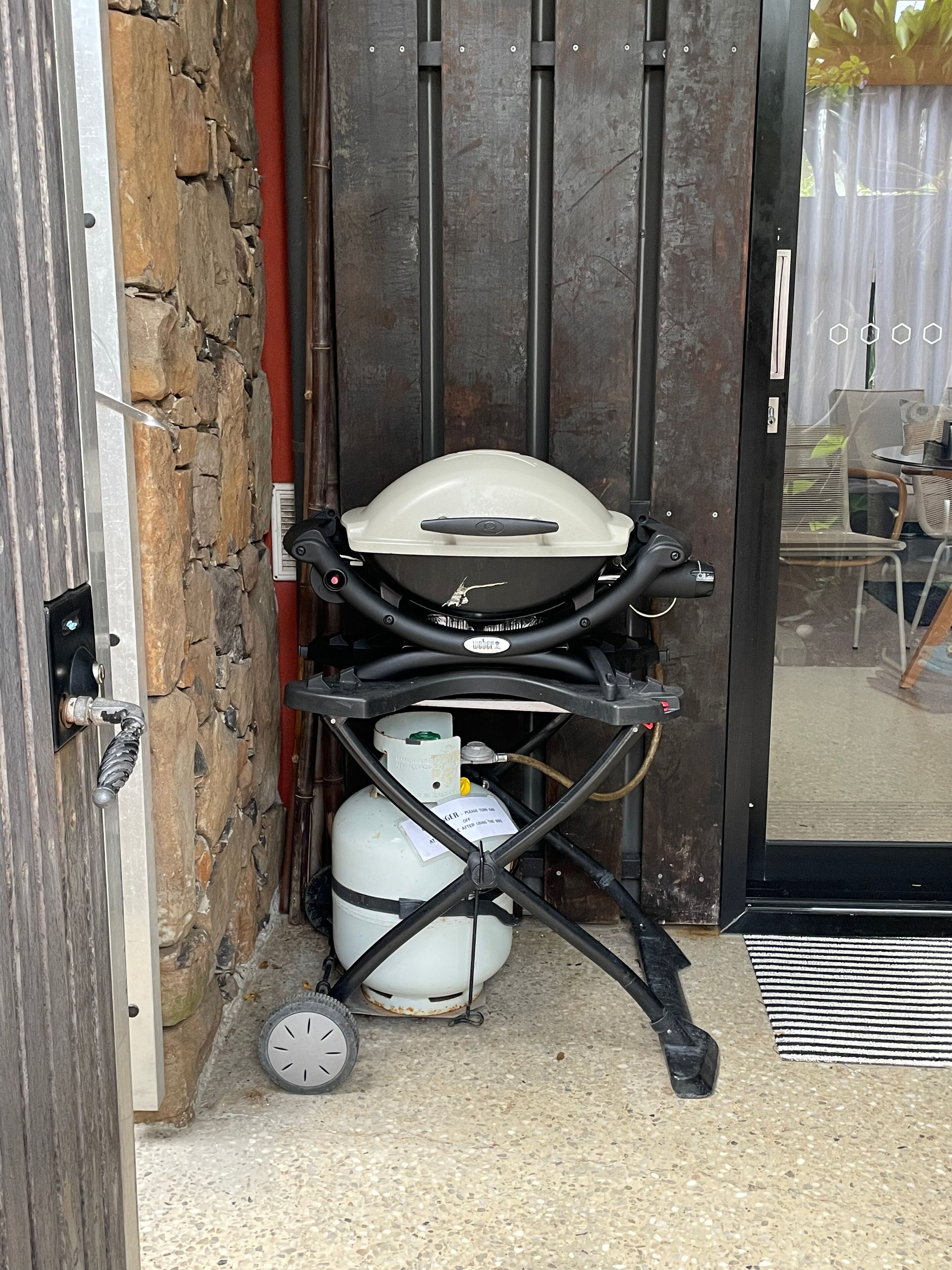 Una parrilla portátil con tanque de propano y un carrito de mano, ubicada en un umbral con pared de piedra y puerta de metal.
