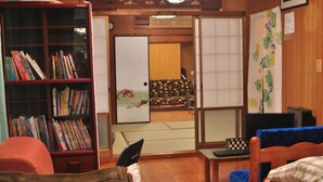 Una habitación tradicional japonesa con suelo de tatami, un separador de ambiente de tatami, una estantería con libros, un pequeño escritorio con un teclado y una cama futón.