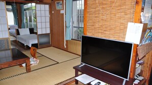 Una habitación tradicional japonesa con suelo de tatami, una mesa de madera baja, un televisor sobre un soporte y una puerta corredera.